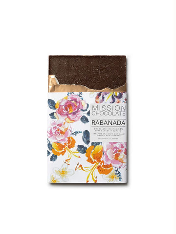 Embalagem do chocolate de rabanada com rosas e flores laranjas sobre o fundo branco. Um pouco do chocolate está para fora, mostrando o açúcar e a canela do chocolate.