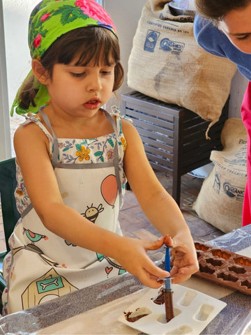 Criança com um lenço sobre a cabeça e um avental tendo aula de como fazer chocolate. 